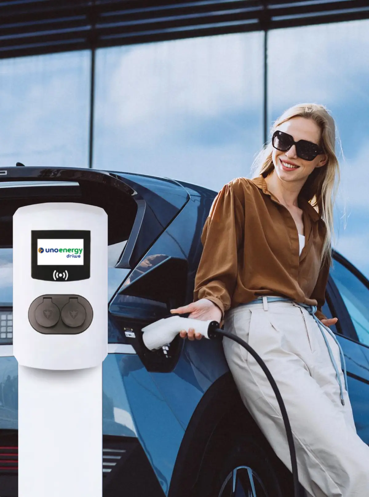 Donna ricarica auto elettrica presso stazione Unoenergy, indossa occhiali da sole e camicetta marrone.