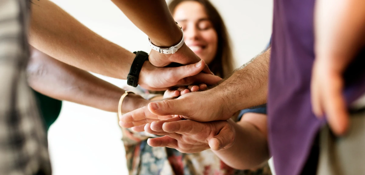 Gruppo di persone che uniscono le mani in un gesto di collaborazione e lavoro di squadra.