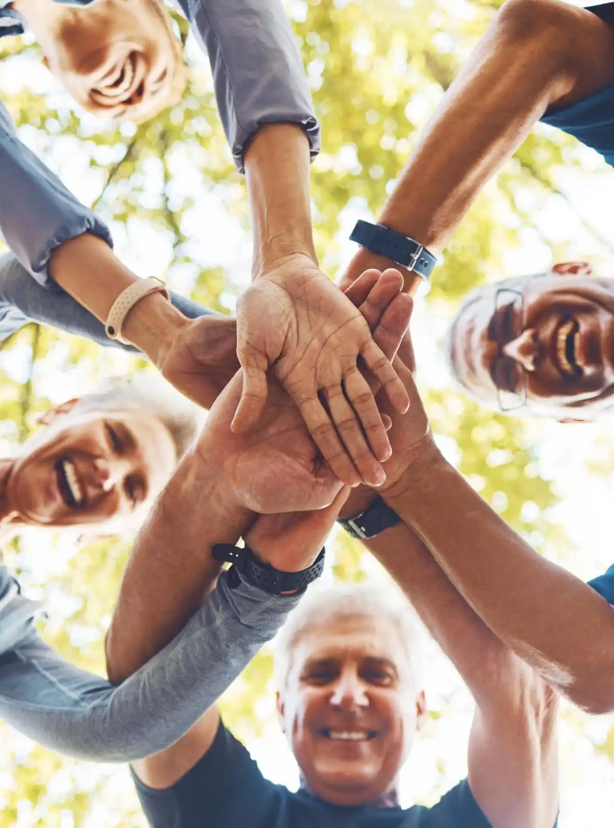 Gruppo di persone anziane che si uniscono con le mani in un gesto di squadra all'aperto.