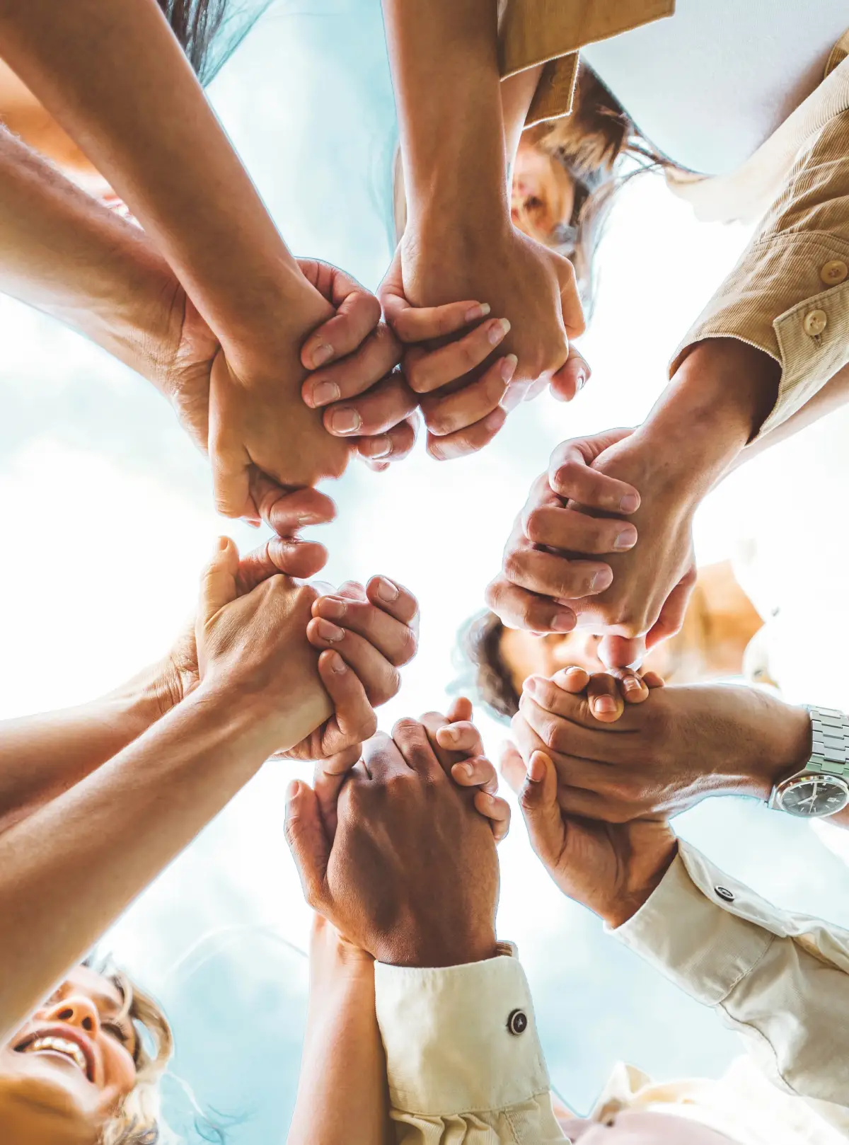 Persone che si tengono per mano in cerchio, viste dal basso, simbolo di unità e collaborazione.