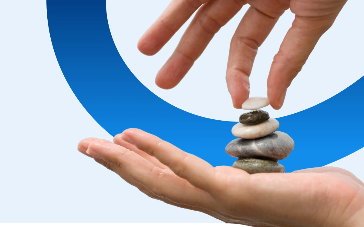 Mani posizionano pietre piatte impilate su sfondo blu.