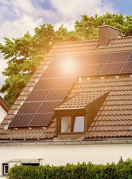 Tetto con pannelli solari su casa, cielo sereno e alberi sullo sfondo.