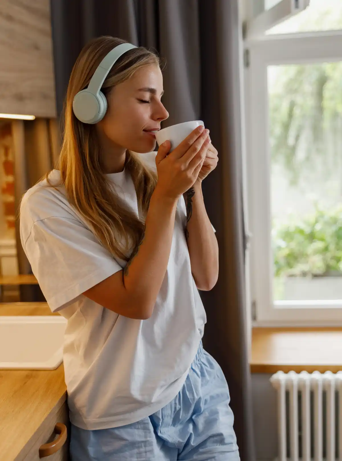 ragazza con occhi chiusi beve da una tazza ascoltando musica