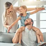 Coppia con bambina gioca sul divano con la luce che entra dalla finestra